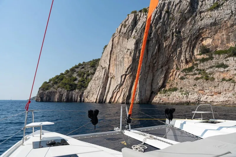  Yacht Photos Pics Catamaran sailing near rocky cliffs, Excess 15, 2023 model, clear blue sea and sky.