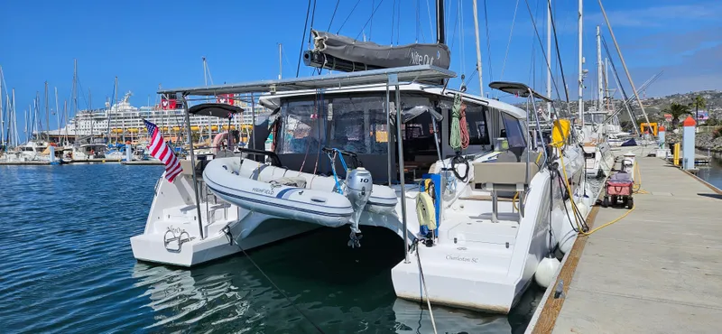 Night Out Yacht Photos Pics 2023 Nautitech 44 Open catamaran docked at a marina with a dinghy and American flag.