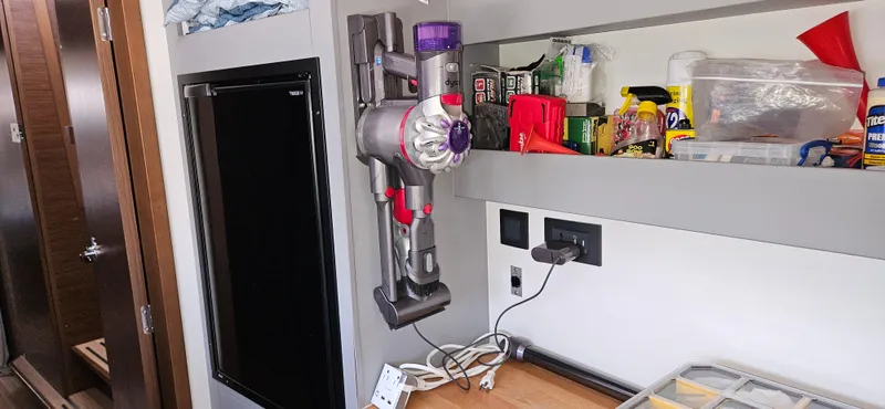 Night Out Yacht Photos Pics Compact storage area in a 2023 Nautitech 44 Open, featuring a mounted vacuum and organized shelves.