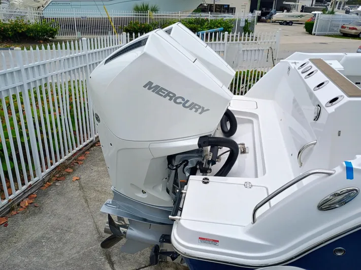 252-449 Yacht Photos Pics 2025 Blackfin 252 CC boat with Mercury outboard engine, docked near a white fence.