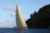 Sailing yacht Devonport Challenge 67, 1995, cruising near a rocky coastline under a clear sky.