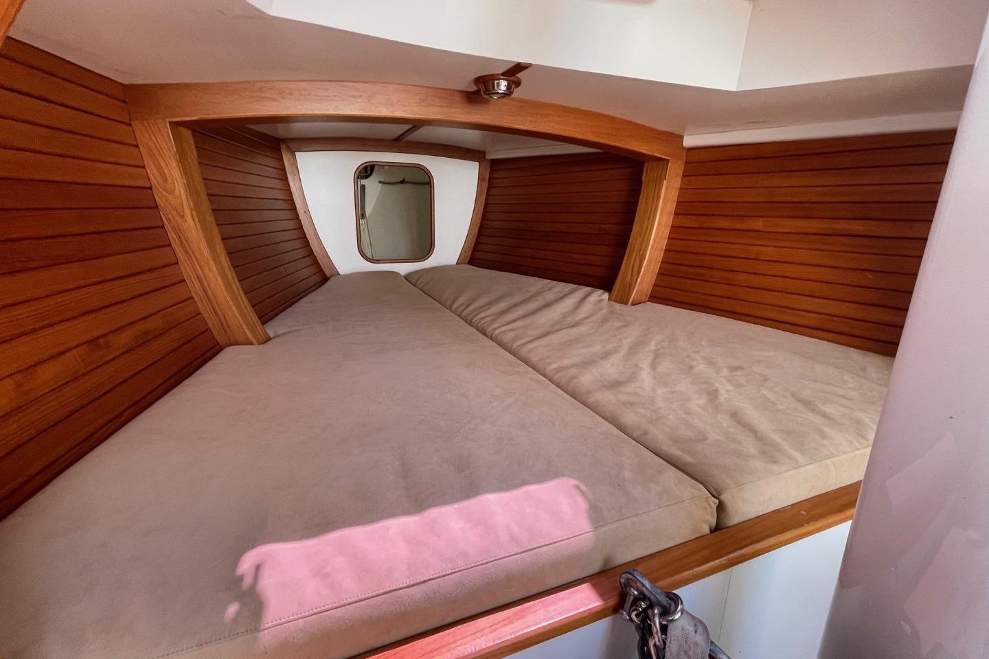 Cozy cabin interior of 2013 Rustler 33 sailboat with wooden paneling and cushioned bed.