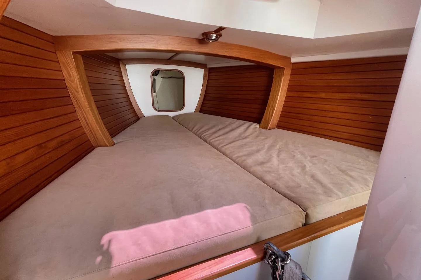 Cozy cabin interior of 2013 Rustler 33 sailboat with wooden paneling and cushioned bed.