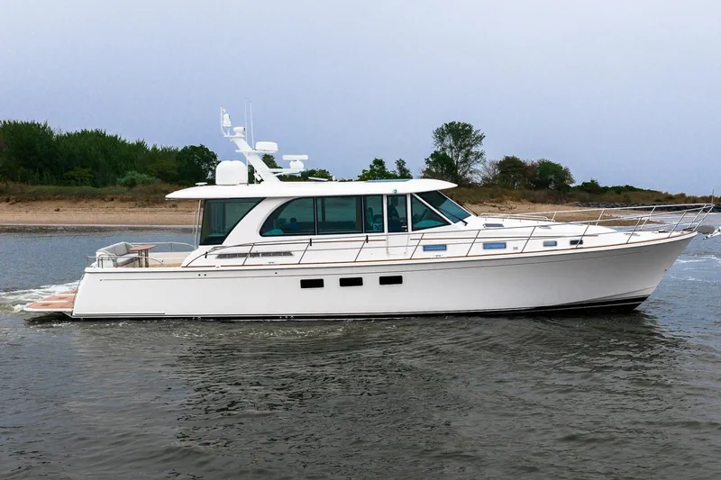  Yacht Photos Pics 2024 Sabre 58 Salon Express yacht cruising on calm waters near a sandy shoreline.