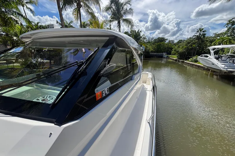  Yacht Photos Pics 2024 Pursuit OS 445 Offshore boat docked on a serene canal, surrounded by lush palm trees.