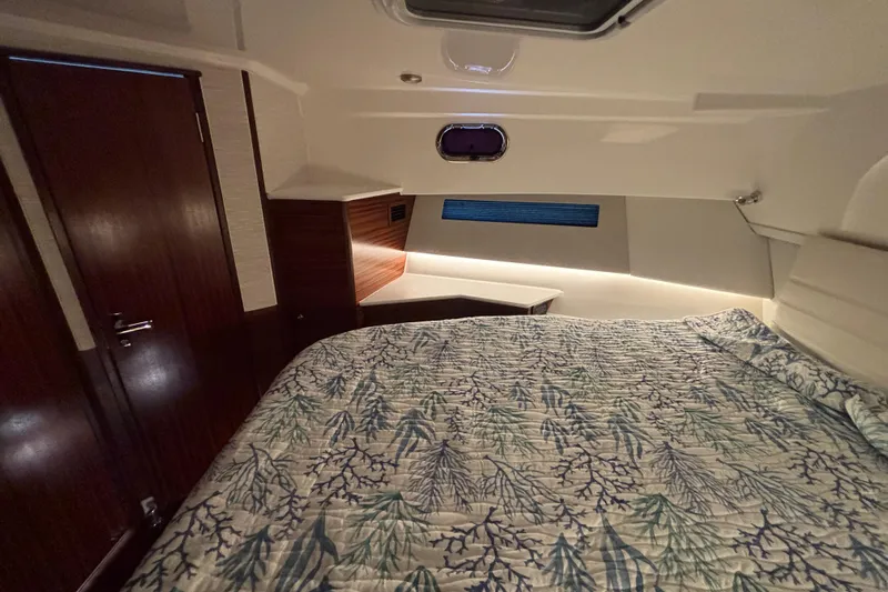  Yacht Photos Pics 2024 Pursuit OS 445 Offshore cabin with bed, wood accents, and ambient lighting.