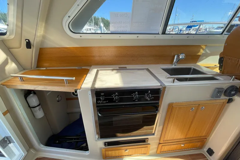 Sweet Jane Yacht Photos Pics Compact kitchen in 2015 Aspen C100 boat with stove, sink, and wooden cabinetry.