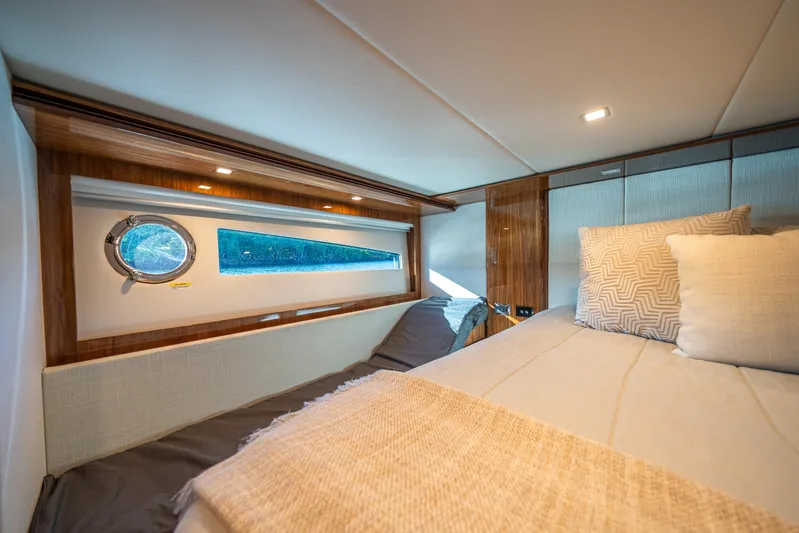 Water Dog Yacht Photos Pics Luxurious cabin interior of 2024 Riviera 5400 Sport Yacht with elegant bedding and porthole view.