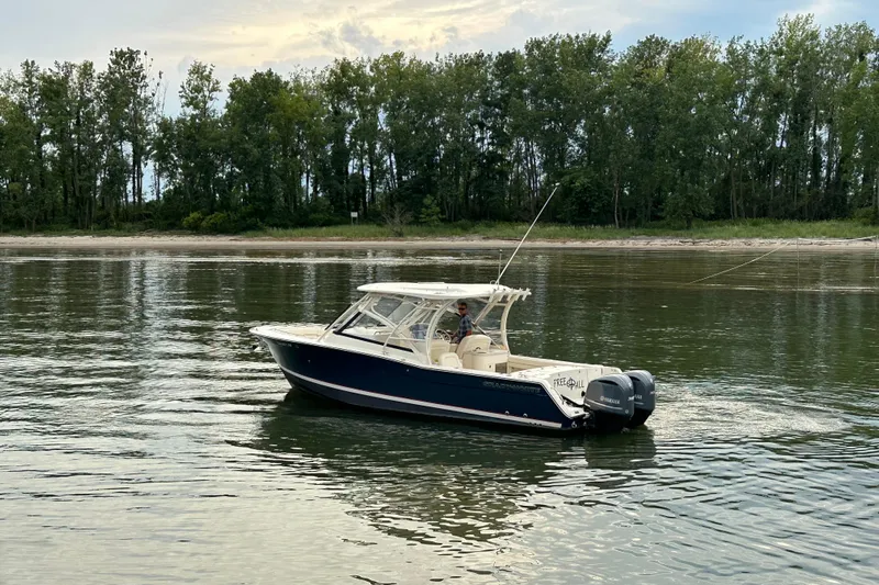  Yacht Photos Pics 2016 Grady-White Freedom 307 boat on calm water near a forested shoreline.
