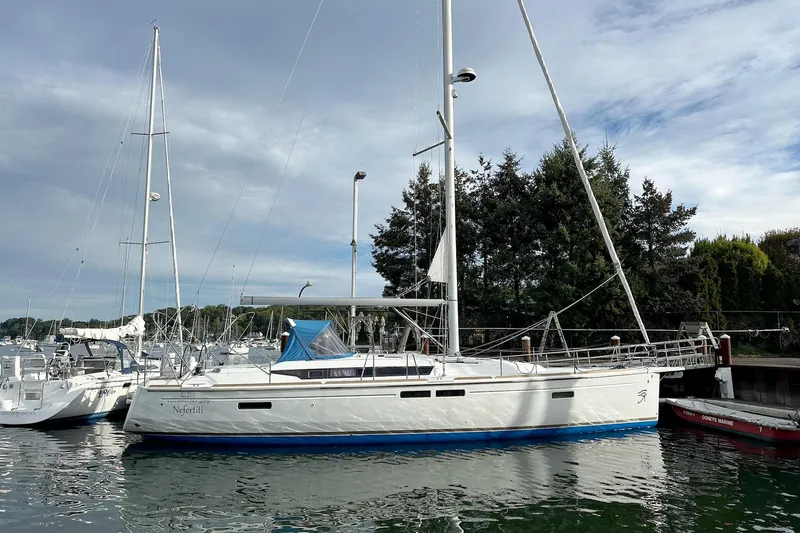  Yacht Photos Pics 2018 Jeanneau Sun Odyssey 479 sailboat docked in a marina, surrounded by trees and calm water.