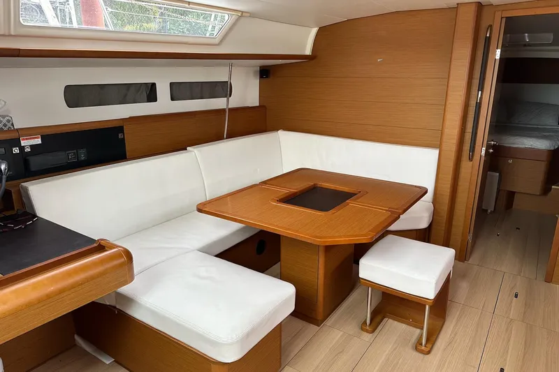  Yacht Photos Pics Interior of 2018 Jeanneau Sun Odyssey 479 yacht with white seating and wooden table.