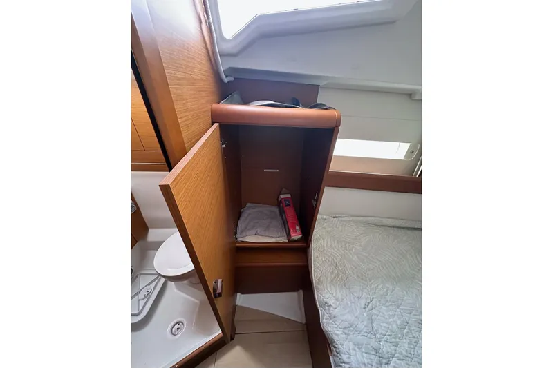  Yacht Photos Pics Interior of 2018 Jeanneau Sun Odyssey 479, featuring a wooden cabinet and cozy bedding.