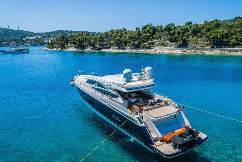 Gitana II Yacht Photos Pics Luxurious 2009 Princess V78 yacht anchored in clear blue waters near a scenic coastline.