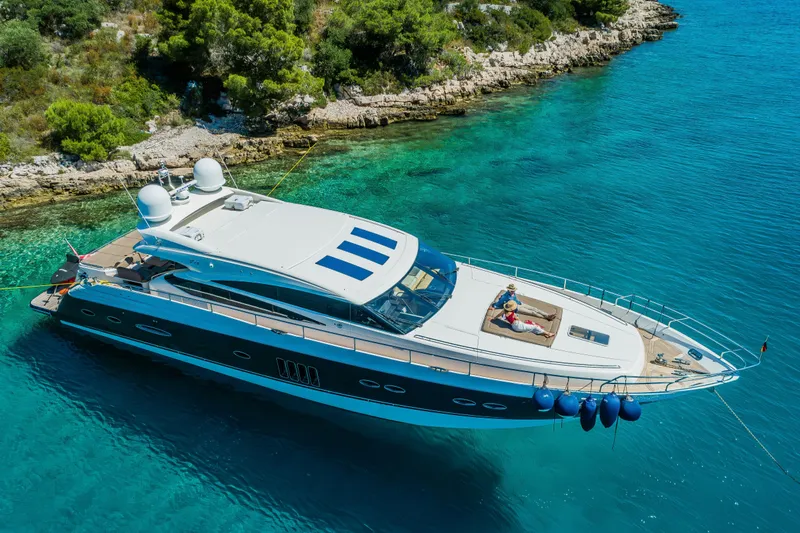 Gitana II Yacht Photos Pics Luxurious 2009 Princess V78 yacht anchored in clear turquoise waters near a rocky shoreline.