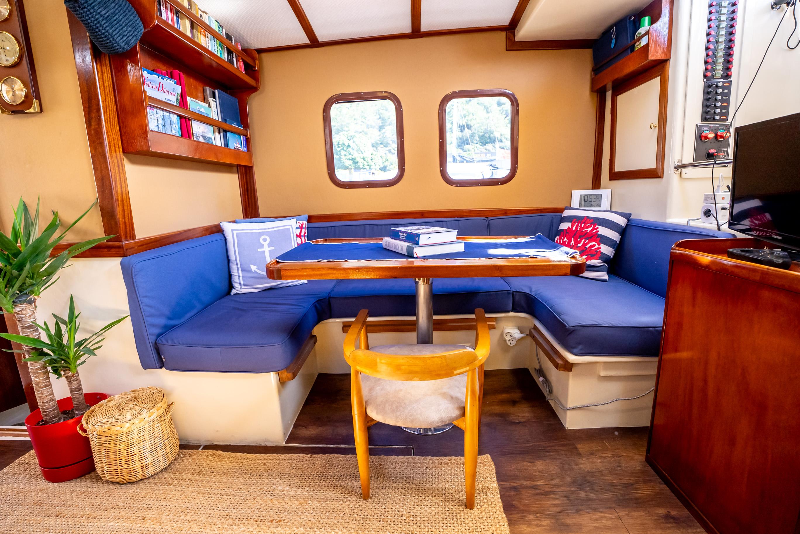 Cozy 2016 custom trawler interior with blue seating, wooden table, and nautical decor.