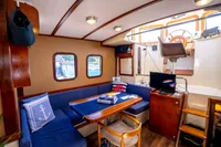 Cozy 2016 custom trawler interior with blue seating, wooden table, and helm station.