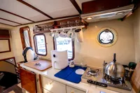 Cozy 2016 custom trawler kitchen with stove, kettle, and porthole window.