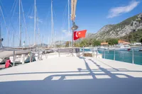 Custom 2016 trawler with Turkish flag docked in scenic marina, surrounded by mountains and sailboats.