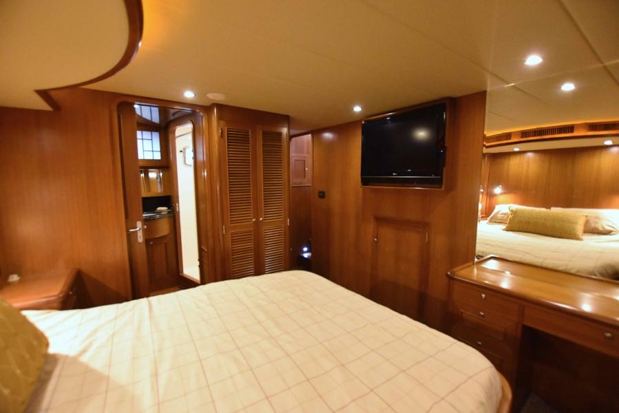 Luxurious bedroom in 2009 Explorer 64' Trawler Grand Alaskan yacht with wood paneling and TV.