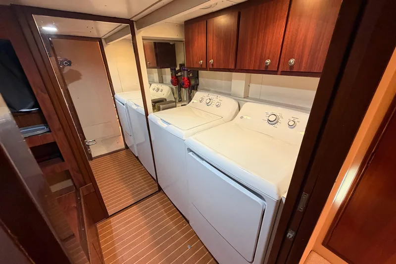  Yacht Photos Pics Laundry area inside 1991 Hatteras 70 Motor Yacht with washer, dryer, and wooden cabinets.