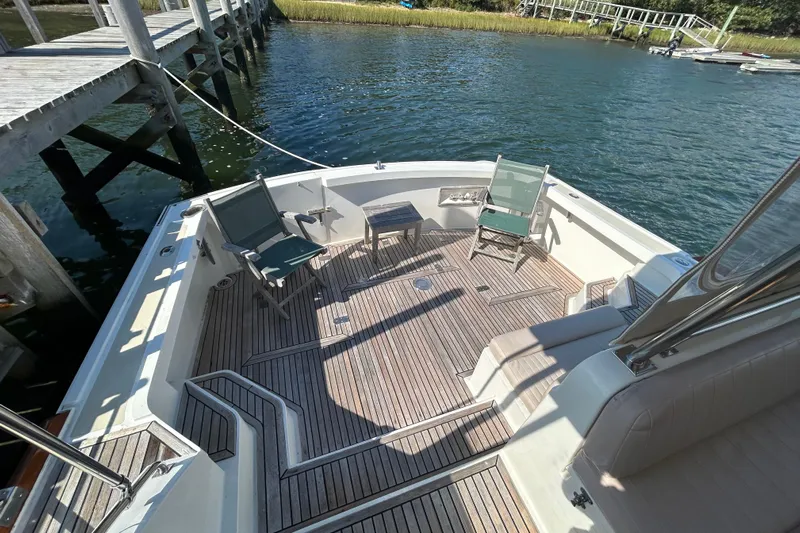 Pearl Yacht Photos Pics 1999 Eastbay 38 boat deck with chairs, table, and wooden flooring by the water.