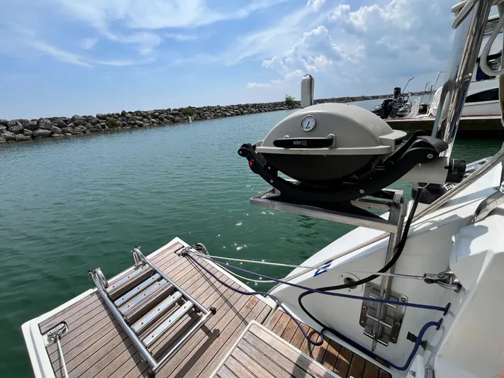 Lali Yacht Photos Pics Beneteau Oceanis 510 CU yacht with a mounted grill, docked by a rocky shoreline.
