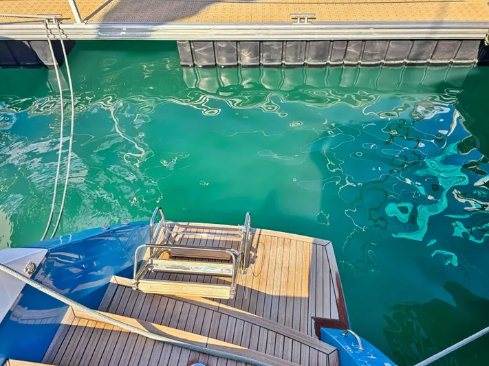 Firefly Yacht Photos Pics Lagoon 620 NEO yacht stern with wooden deck, docked in clear turquoise water.