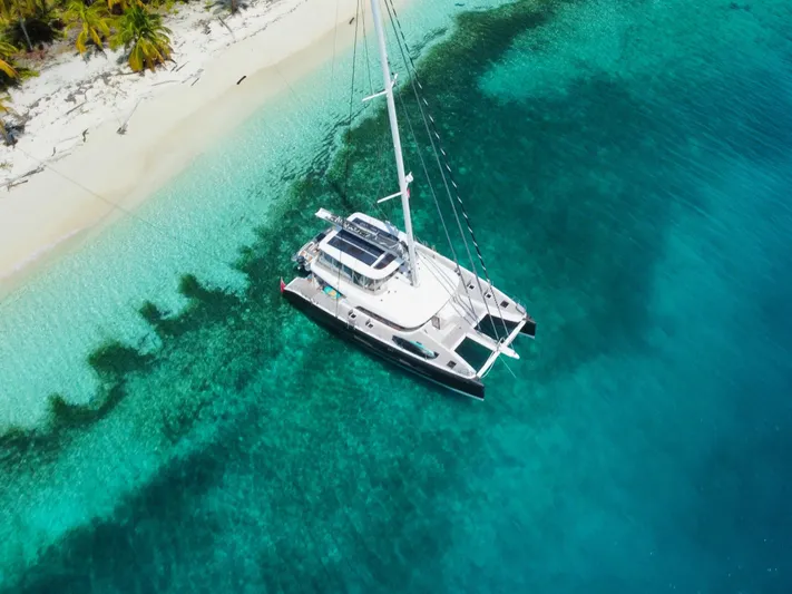 Big Picture Yacht Photos Pics 2024 Lagoon SIXTY 5 catamaran anchored near tropical beach with clear turquoise water.
