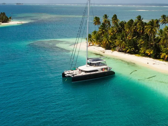 Big Picture Yacht Photos Pics 2024 Lagoon SIXTY 5 catamaran anchored near tropical island with palm trees and turquoise waters.