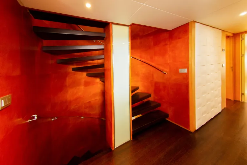  Yacht Photos Pics Luxurious yacht interior with modern spiral staircase, dark wood flooring, and vibrant orange walls.