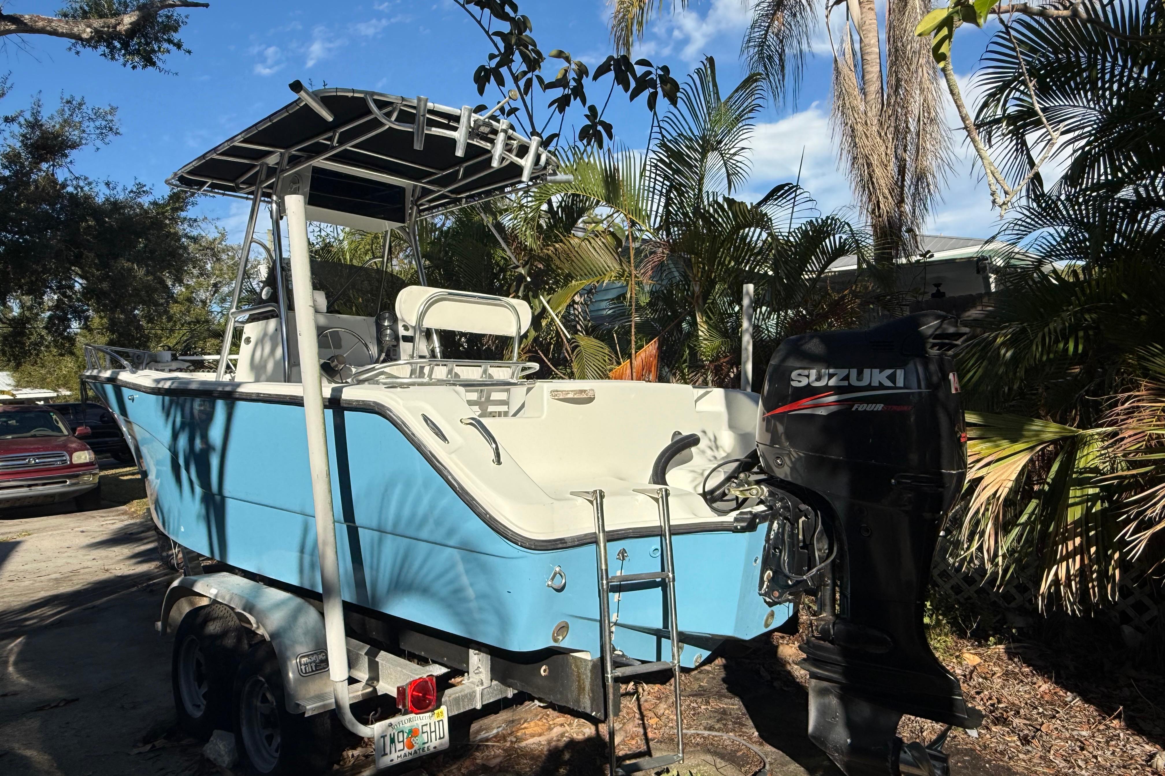 Blue 2002 Fishmaster 212 Travis Edition boat with Suzuki outboard motor, parked outdoors.