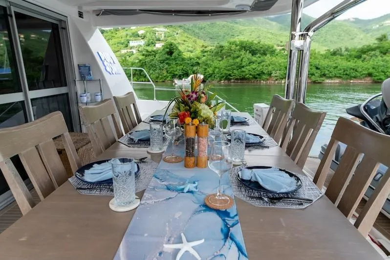 Ruby One Yacht Photos Pics Elegant dining setup on Leopard 58 yacht, 2020, with scenic water and greenery backdrop.