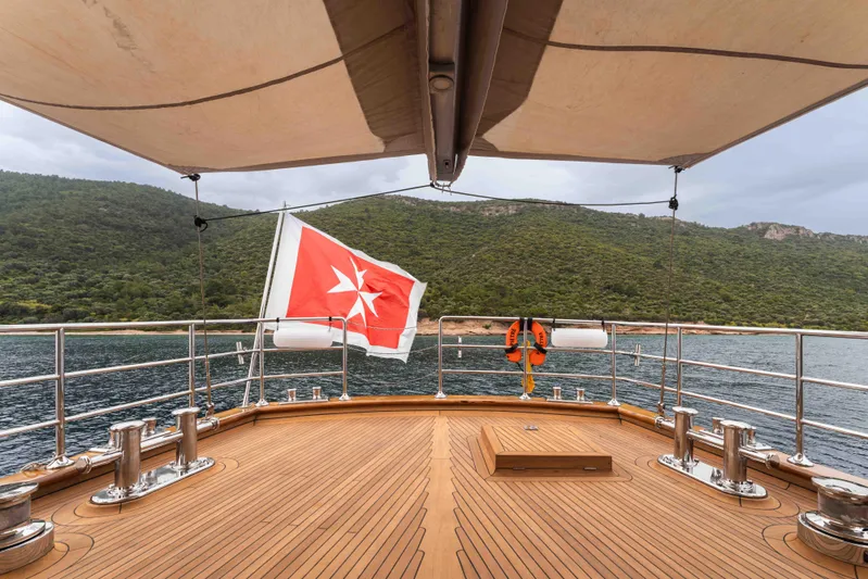 Le Pietre Yacht Photos Pics Custom 2009 sailing yacht deck with Maltese flag, overlooking serene coastal landscape.