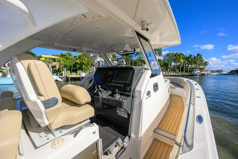 Leap Year Yacht Photos Pics 2018 Pursuit S 408 Sport boat interior with helm, beige seating, and waterfront view.