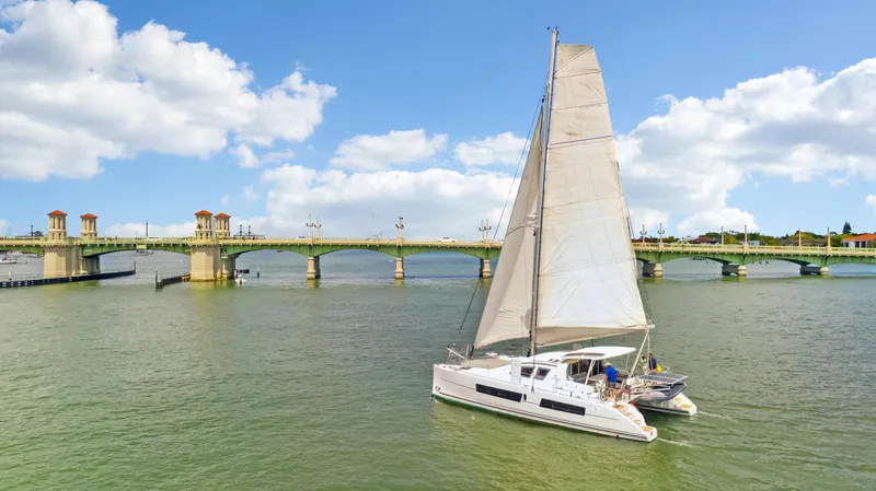 Zephyr Yacht Photos Pics Catana 42 sailboat cruising near a scenic bridge under a partly cloudy sky.