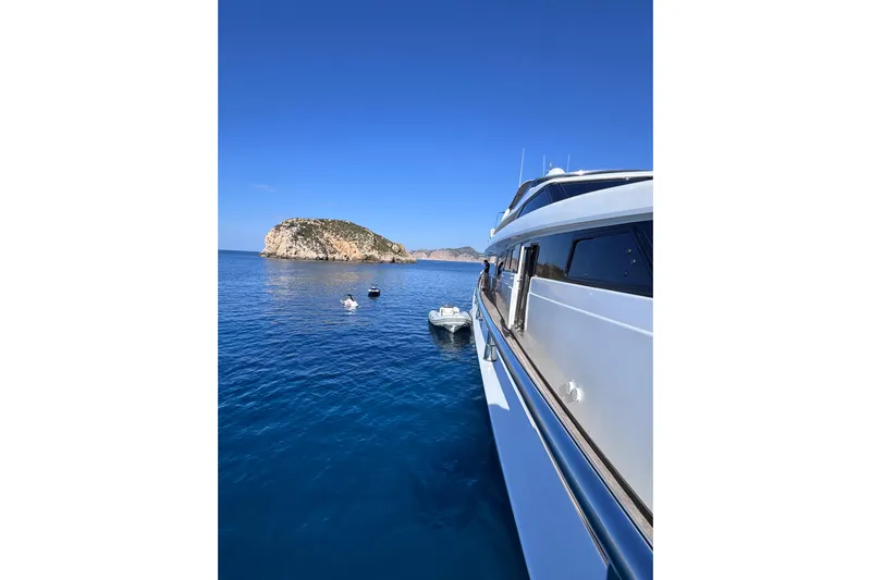  Yacht Photos Pics Sanlorenzo SL88 yacht from 2000 on serene blue waters near a rocky island.