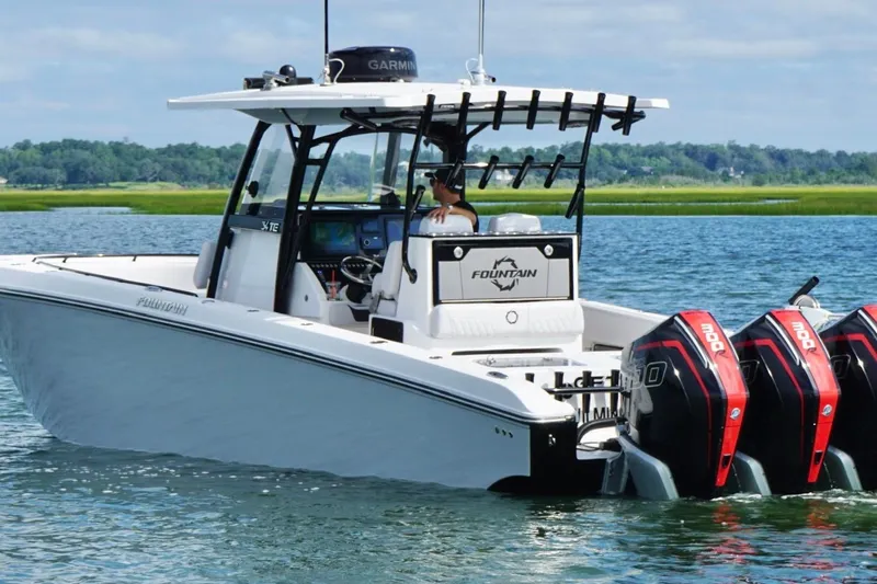  Yacht Photos Pics 2024 Fountain 34 TE boat with triple outboard engines on a serene waterway.