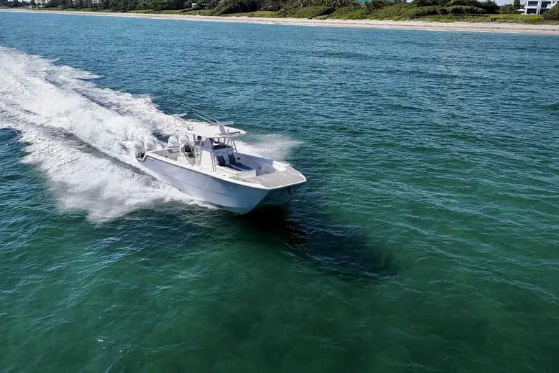 Little Lady Yacht Photos Pics 2024 Invincible 35 Catamaran cruising on clear blue ocean near a sandy shoreline.