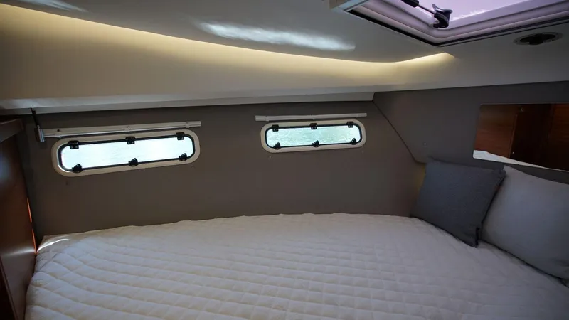 In-stock 2024 Nimbus 305 Coupé #393 Yacht Photos Pics Cozy cabin interior of 2024 Nimbus 305 Coupe #393 with porthole windows and bedding.
