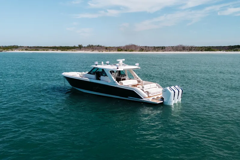 Phoenix Yacht Photos Pics 2023 Tiara 48 yacht cruising on serene blue waters near a sandy shoreline.