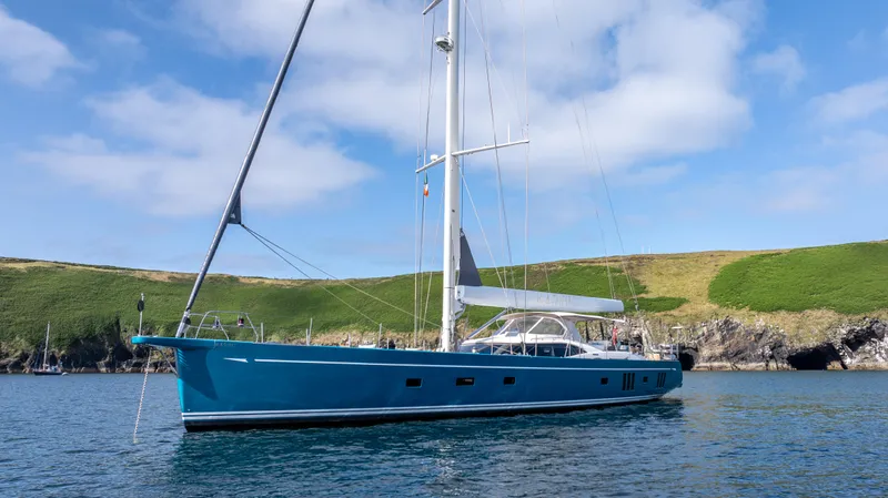 Karibu Yacht Photos Pics Luxurious 2013 Oyster 885 yacht sailing near a scenic, grassy coastline under a blue sky.