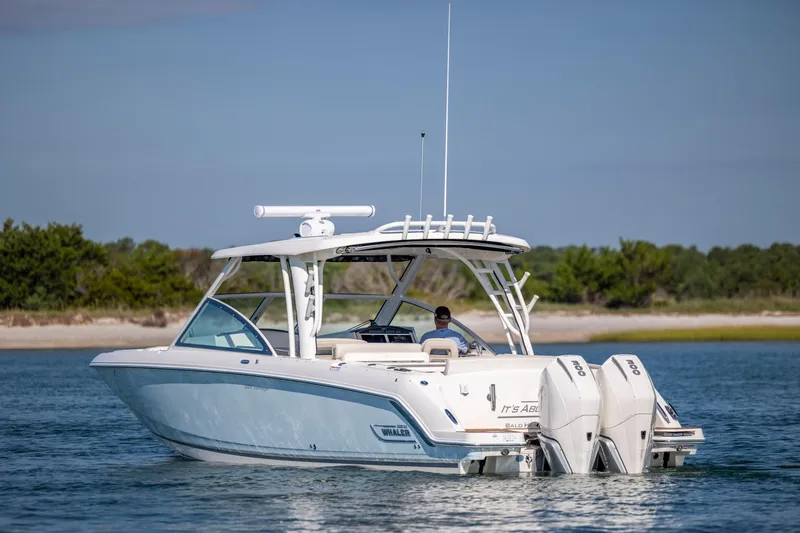  Yacht Photos Pics 2023 Boston Whaler 320 Vantage boat cruising on calm waters near a sandy shoreline.
