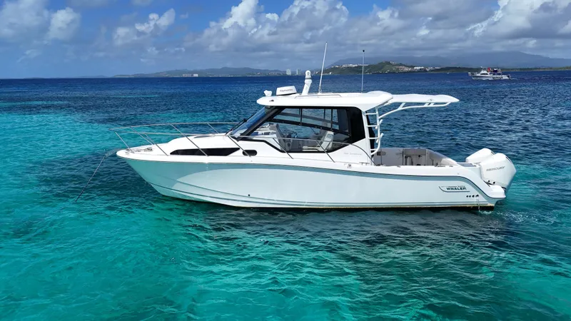  Yacht Photos Pics 2020 Boston Whaler 325 Conquest boat on clear turquoise water, under a partly cloudy sky.
