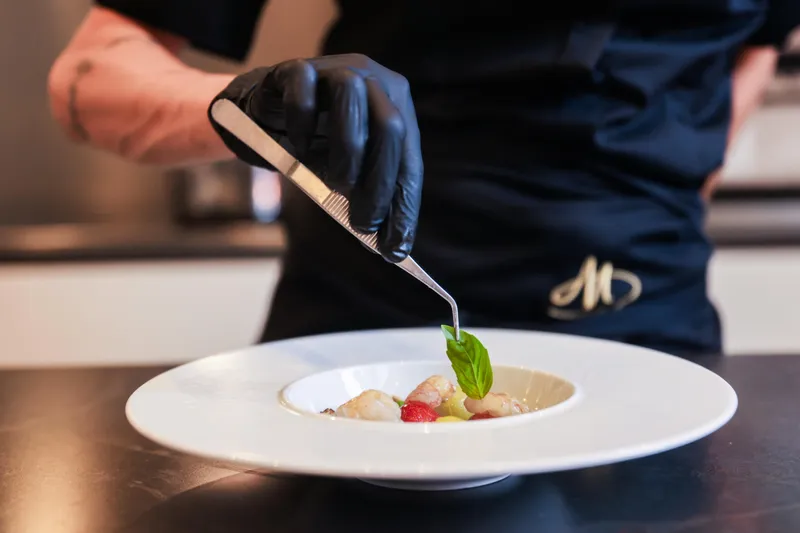 Millesime Yacht Photos Pics Chef garnishing dish with basil leaf using tweezers, wearing black gloves.