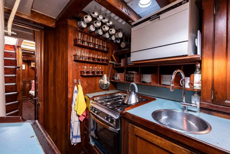Juliette Yacht Photos Pics 1929 Robertson boat kitchen with wooden cabinetry, stove, sink, and dishware storage.