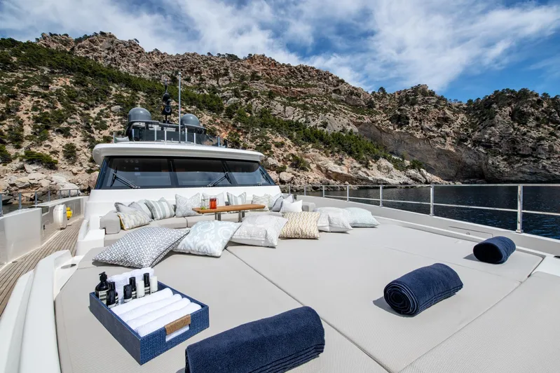Mac One Yacht Photos Pics Luxurious 2019 Custom Line Navetta 33 yacht with sunbathing area, cushions, and towels, near rocky coastline.