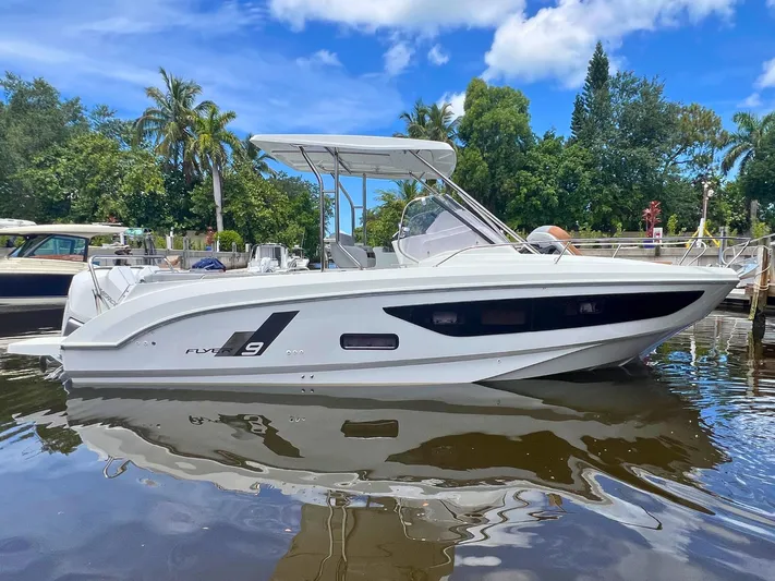  Yacht Photos Pics 2025 Beneteau Flyer 9 SUNdeck boat docked on calm water, surrounded by lush greenery.