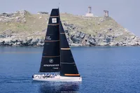 Sailing yacht TP52 from 2007 gliding near rocky coastline under clear skies.