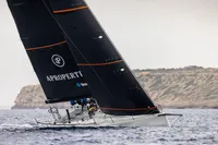 Sailing yacht TP52 from 2007 gliding on the sea near rocky coastline.