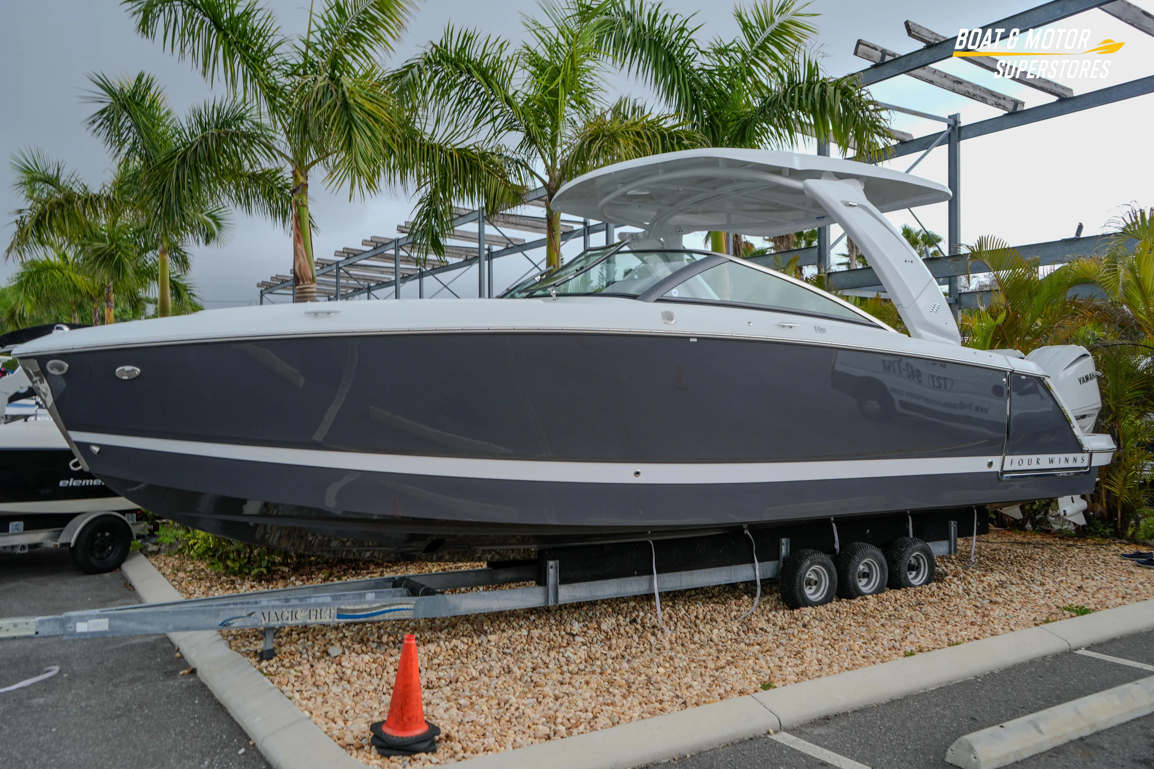 2026 Four Winns H9 OB boat on trailer, surrounded by palm trees.